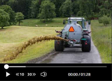 Un tracteur roule le long d'une route de campagne et déverse du lisier.