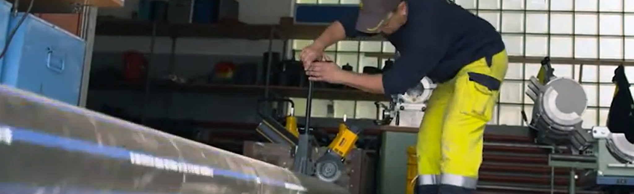 Un monteur de tuyauterie travaille sur une machine dans une usine avec du texte.